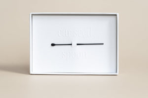 Minimalist white packaging displaying a black spoon tool accessory for ear seeds, part of The Foundation - 24K Gold Ear Seed | Vie Healing wellness product.