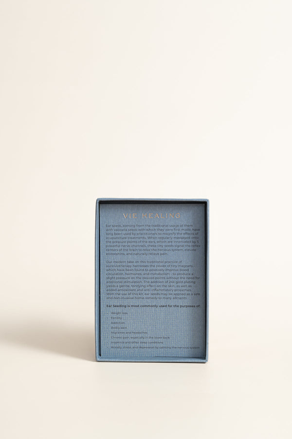 Blue box packaging with detailed product description text for Calm Cool Collected - 24K Gold Ear Seed | Vie Healing, promoting wellness through traditional ear seed therapy.