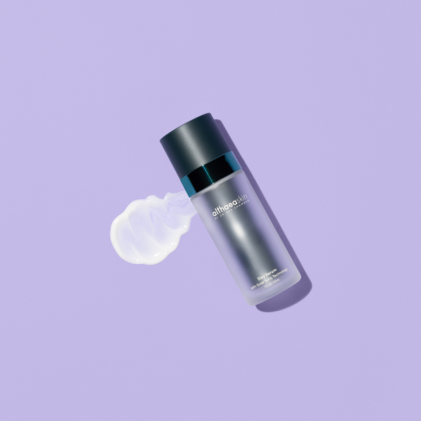 Day Serum | Althaea Skin bottle with a smooth white serum texture spread beside it on a purple background, showcasing skincare product designed for daily use.