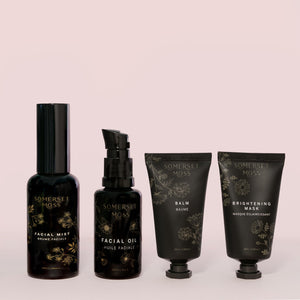 Collection of four skincare products in black packaging labeled Discovery Kit | Somerset Moss, featuring facial mist, facial oil, balm, and brightening mask on a pale pink background.