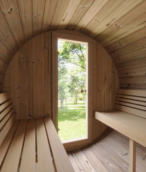 Interior view of the wooden barrel-shaped sauna with benches on either side and a glass door opening to a green outdoor landscape, showcasing the E7W Barrel Sauna - 4 Person | Western Sol.