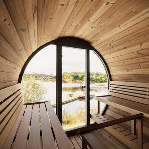 Interior view of EE8G Sauna Barrel - 6-8 Person | Western Sol with wooden benches and large glass door overlooking a peaceful lake and natural landscape for wellness and relaxation.