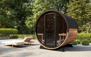 EE8G Sauna Barrel - 6-8 Person | Western Sol outdoor wooden barrel sauna with glass door, set on a patio surrounded by lush greenery and lounge chairs for wellness and relaxation.