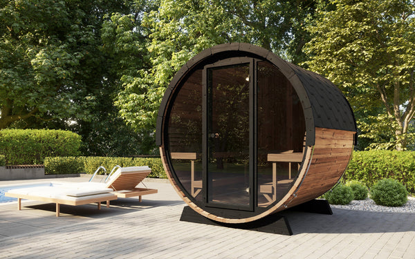 EE8G Sauna Barrel - 6-8 Person | Western Sol outdoor wooden barrel sauna with glass door, set on a patio surrounded by lush greenery and lounge chairs for wellness and relaxation.
