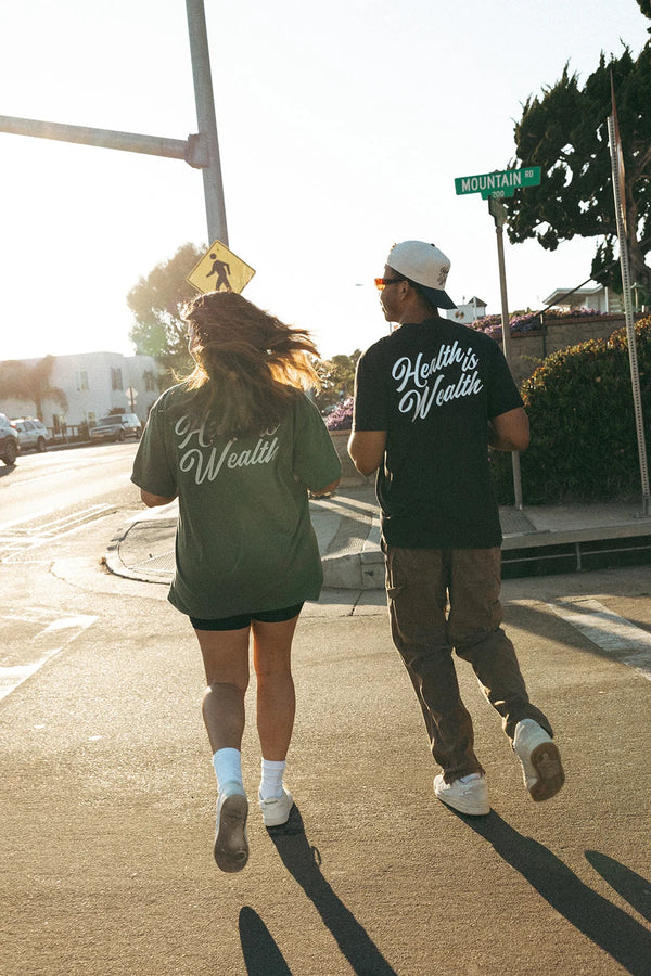 Unisex Health Is Wealth T-Shirt - Private Label | Lucky Owl shown on two people walking outdoors in matching dark shirts with Health Is Wealth script lettering