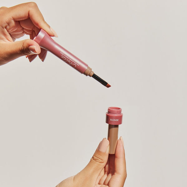 Hands holding an eyebrow cream applicator and matching container in a warm blonde shade for precise brow grooming featuring Eyebrow Cream | Chella.
