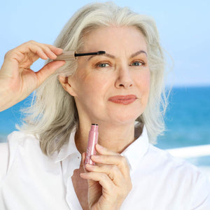 Mature woman applying Eyebrow Defining Gel Clear | Chella to her eyebrows outdoors near the ocean, showcasing a natural skincare and wellness routine.