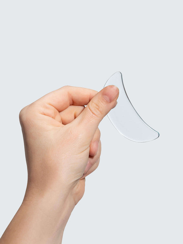 Hand holding a clear curved silicone patch designed for skincare use, part of the SiliconeFusion™ Eyes & Mouth Patches | Dermaclara collection.