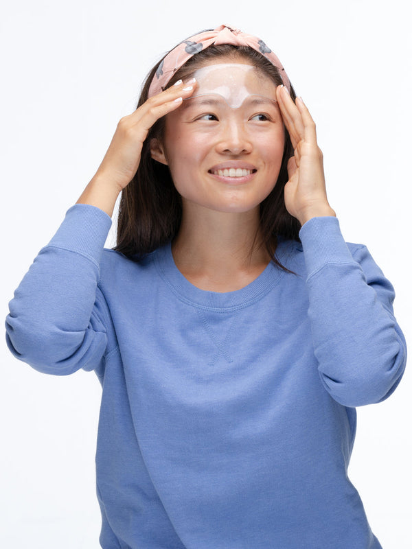 Woman wearing a pink headband gently applying SiliconeFusion™ Forehead Patch | Dermaclara to her forehead as part of a skincare routine for wrinkle reduction and wellness.
