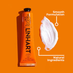 Orange tube of Linämel Toothpaste | LINHART next to a smooth white toothpaste smear labeled with smooth formulation and natural ingredients on an orange background.