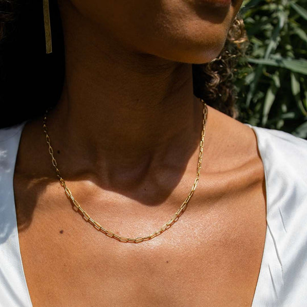 Close-up of a person wearing the Frolic Paperclip Necklace /silver tone | Purpose Jewelry, featuring a delicate silver-tone chain with paperclip links against a natural outdoor background.