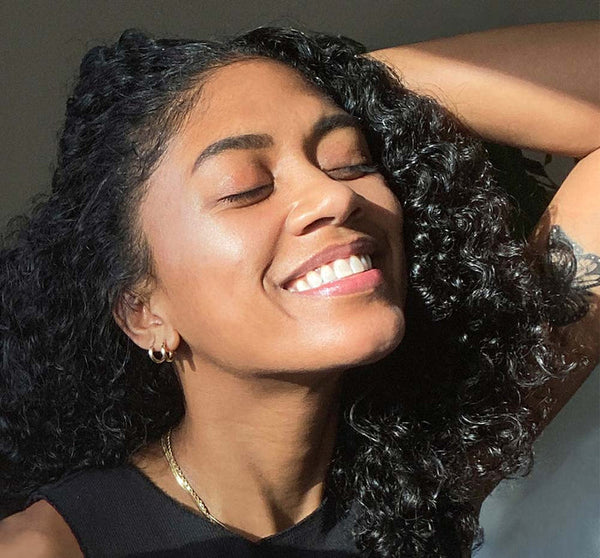 A smiling woman with glowing, radiant skin enjoys sunlight on her face, representing the nourishing benefits of Full Moon Dip® Iridescent Illumination Ageless Facial Mousse with Peptides + Retinol | Farmhouse Fresh skincare.
