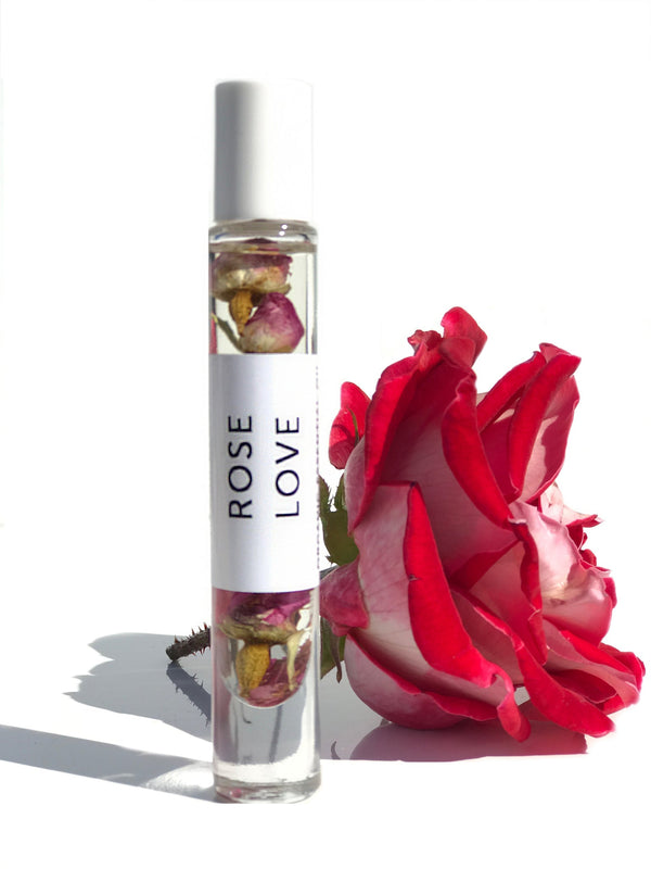 Clear glass roll-on bottle with dried rose petals inside next to a fresh pink and white rose, featuring the label Rose Love Organic Perfume Roll-on | Hydra Bloom
