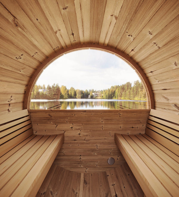 Interior view of the E6W Barrel Sauna - 3 Person | Western Sol showing natural wood seating and a large half-moon window overlooking a calm lake surrounded by trees.