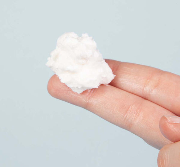 A close-up of a hand holding a small amount of white creamy texture representing Harvest Moon Dip® | FarmhouseFresh skincare product on fingertips.