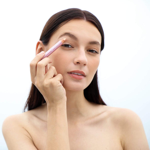 Woman applying makeup with Highlighter Pencil | Chella on her eyebrow area, demonstrating a natural skincare and beauty routine.