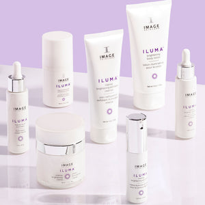 Close-up of various skincare products from IMAGE Skincare’s ILUMA® line arranged on a light purple surface, featuring the ILUMA® intense brightening serum | IMAGE Skincare bottle prominently in the foreground.