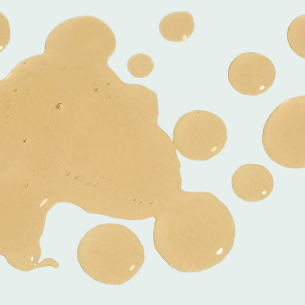 Close-up of golden liquid drops on a light background, representing the texture of ILUMA intense facial illuminator | IMAGE Skincare skincare product.