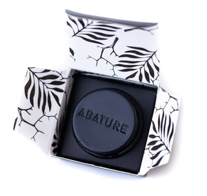 Black circular wellness device embossed with ABATURE, presented in an open box with a white and black leaf pattern, showcasing the Abature Mini | Abature for body care and recovery.