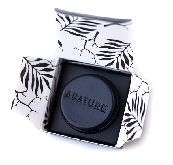 Black circular wellness device embossed with ABATURE, presented in an open box with a white and black leaf pattern, showcasing the Abature Mini | Abature for body care and recovery.