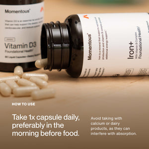 Open bottle of Iron+ capsules lying on its side with capsules spilling out, accompanied by a Vitamin D3 bottle in the background and usage instructions for taking one capsule daily before food.