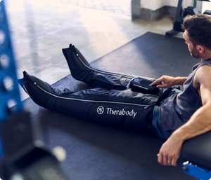 Man using JetBoots Prime | Therabody leg recovery device in a gym setting, demonstrating wellness and recovery therapy after exercise.