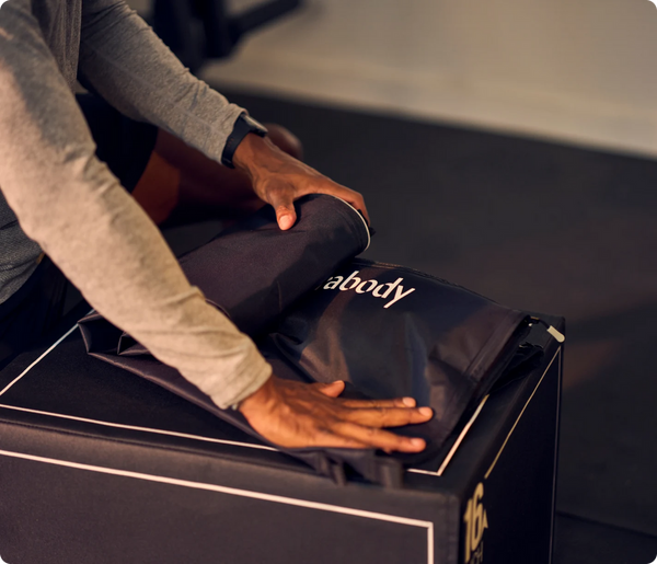 Person unfolding black recovery boots with the logo visible, preparing to use JetBoots Prime | Therabody wellness device for leg recovery and body care.