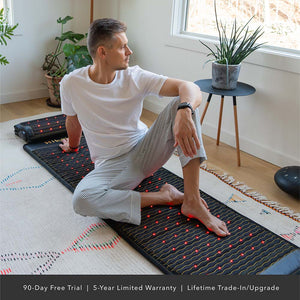 Man seated on Jet Series - PEMF Far Infrared Heating Mats | HealthyLine in a bright room with natural light, stretching and relaxing on the wellness device.