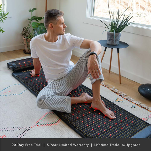 Man seated on Jet Series - PEMF Far Infrared Heating Mats | HealthyLine in a bright room with natural light, stretching and relaxing on the wellness device.
