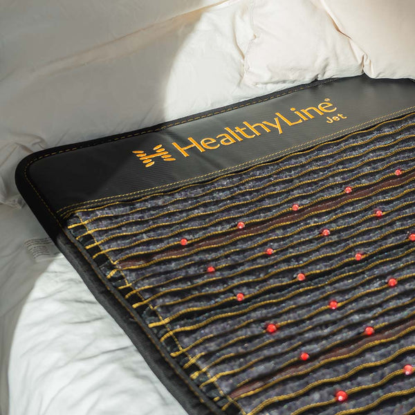 Jet Series - PEMF Far Infrared Heating Mats | HealthyLine laid out on a bed with visible red therapy points and textured stitching, promoting wellness and recovery.