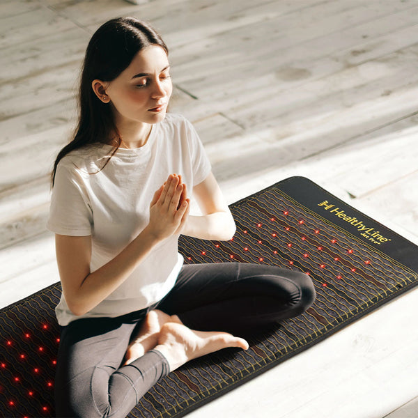 Woman practicing meditation on a black Jet Series - PEMF Far Infrared Heating Mats | HealthyLine, featuring red light therapy nodes for enhanced wellness and recovery.