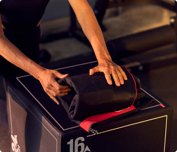 Person folding a black and red recovery device on a workout box, showcasing the JetBoots PRO Plus | Therabody wellness tool designed for enhanced body care and recovery.