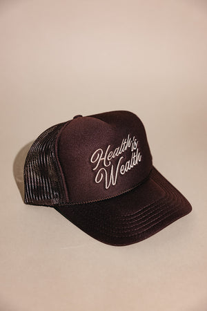 Black mesh-backed trucker hat with white embroidered "Health is Wealth" slogan on the front, styled for casual wellness and outdoor fashion, named Health is Wealth Trucker Hat | Lucky Owl.