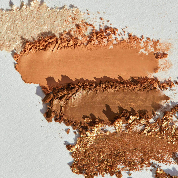 Close-up of warm-toned beige, copper, bronze, and shimmery gold eyeshadow swatches from La Vie Neutral Eyeshadow Palette | Chella on a white surface.