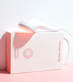 LightStim For Wrinkles | LightStim handheld skincare device emitting red light therapy, resting on its white and pink packaging box promoting wrinkle reduction.
