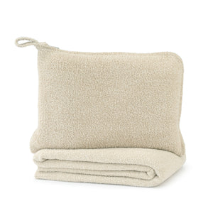 Travel Set (Blanket, Socks, Eyemask, Bag) | Kashwére featuring a soft, beige textured pouch resting on a folded matching blanket designed for comfort and wellness during travel.