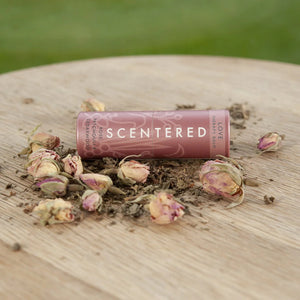 Love Therapy Balm | Scentered in a rose-colored tube surrounded by dried rosebuds and natural botanical elements on a wooden surface, highlighting skincare and wellness.