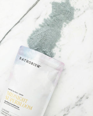 Midnight Superbloom Crush | Bathorium bath soak pouch resting on white marble with a soft gray powder spill and pastel packaging details visible