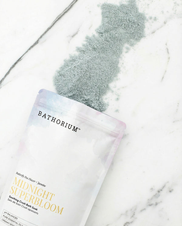 Midnight Superbloom Crush | Bathorium bath soak pouch resting on white marble with a soft gray powder spill and pastel packaging details visible