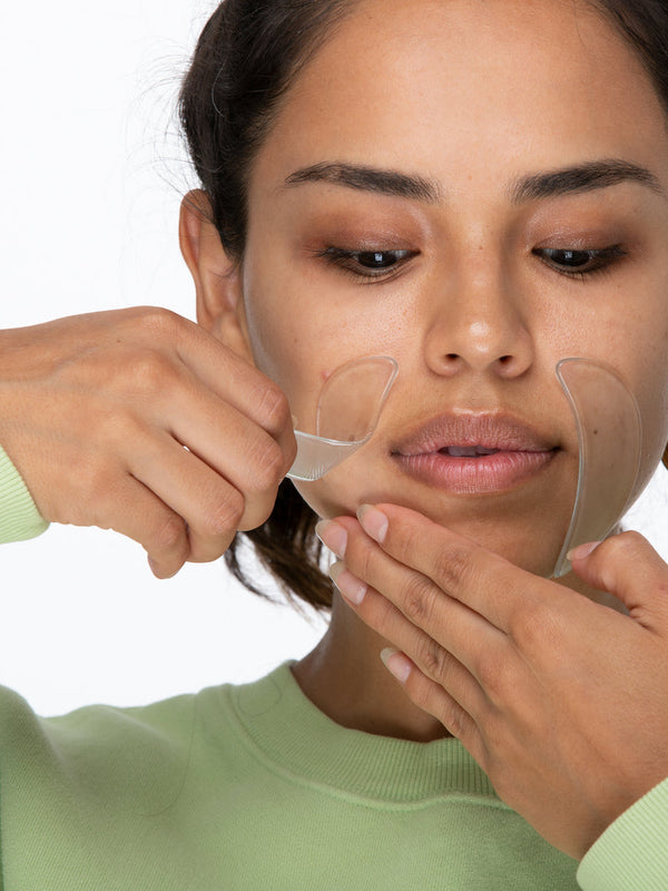 A woman applies SiliconeFusion™ Eyes & Mouth Patches | Dermaclara near her mouth, demonstrating the clear silicone patches designed for skincare and wrinkle reduction.