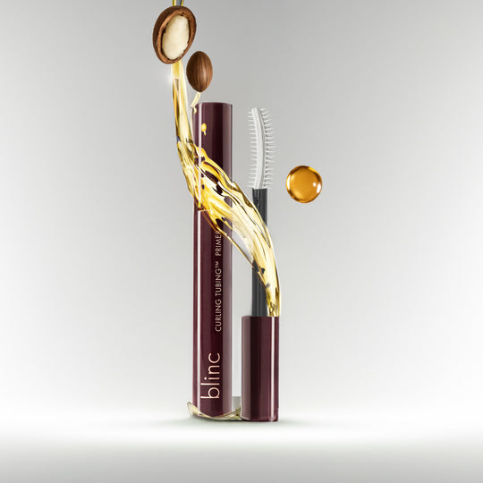 Curling TUBING™ Primer | Blinc with a sleek dark maroon tube, shown with oil droplets and natural nut ingredients, highlighting skincare and beauty wellness benefits.
