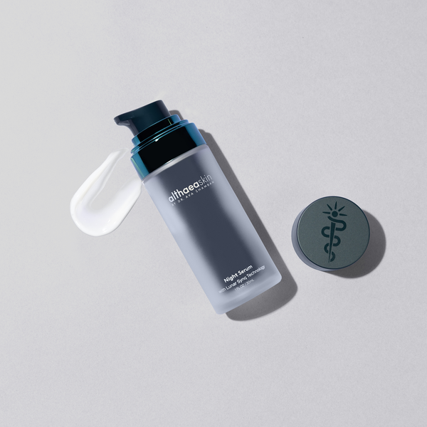 Bottle of Night Serum | Althaea Skin with a swirl of white serum next to a round cap featuring a medical symbol, displayed on a light gray surface for skincare and wellness.