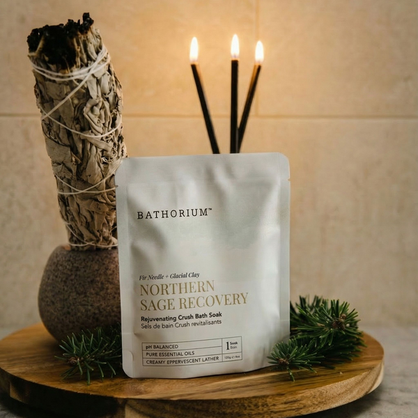 Northern Sage Recovery Crush | Bathorium pouch of rejuvenating crush bath soak on a wooden tray with a sage bundle pine sprigs and lit candles