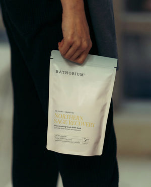 Northern Sage Recovery Crush | Bathorium resealable pouch held by a person in dark clothing showing the Bathorium label and Northern Sage Recovery blend for bath care