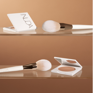 Bronzing Powder Brush | NUDA with soft white bristles and a sleek white handle, displayed alongside a compact bronzing powder in a minimalistic setting.