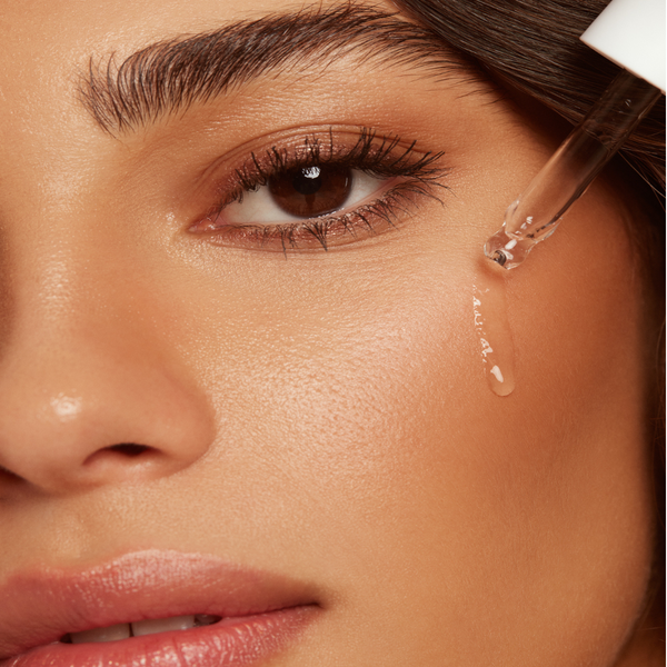 Close-up of a woman applying Hyaluronic Self Tanning Serum | NUDA to her cheek with a dropper, highlighting smooth, glowing skin and skincare application.
