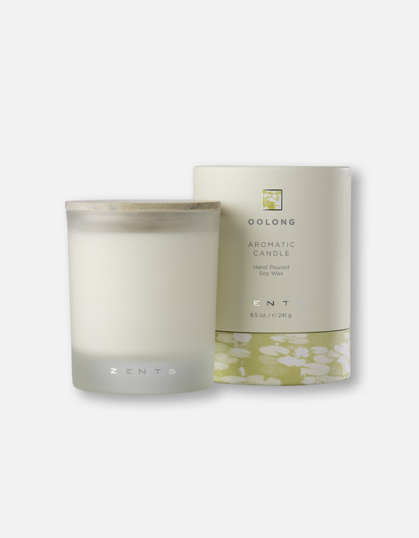 A frosted glass Aromatic Candle | Zents with a wooden lid next to its minimalist beige packaging featuring delicate floral design accents.