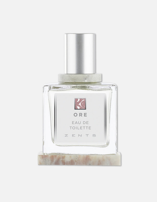 Clear glass bottle of Eau de Toilette | Zents with a silver cap, minimalist label, and light neutral-toned marble base, showcasing a clean and elegant design.