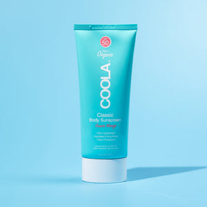 Classic Body Organic Sunscreen Lotion SPF 50 - Guava Mango | COOLA in a turquoise tube against a light blue background, featuring organic skincare designed for lightweight hydration and sun protection.