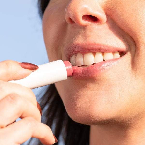 A person applying Classic Liplux® Lip Balm Tinted SPF 30 | COOLA with a soft pink tint on their lips, showcasing skincare and lip wellness.